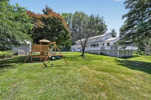 Ein Garten mit einer Holz-Schaukel, einem weißen Zaun und einem Haus mit Veranda.