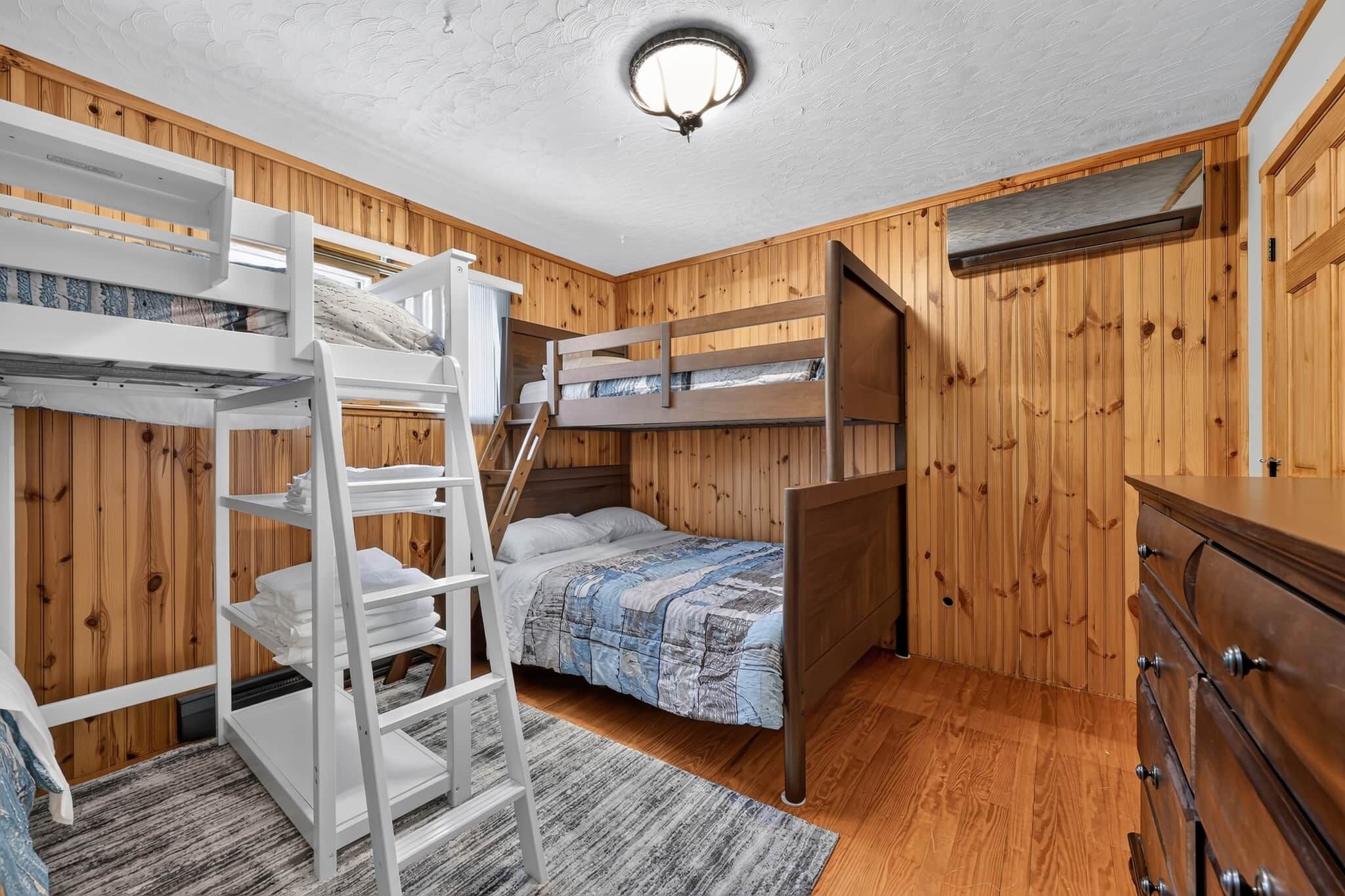 Une chambre avec un lit superposé, des murs en bois, une commode et un luminaire au plafond.