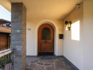 A stone-paved entrance with a wooden door, a mailbox, and a number '46' on the wall. - Villa zur Gondel (Waidring)