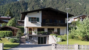 Eine zweistöckige Chalet mit Natursteinfassade, einem mit Pflanzen bepflanzten Balkon und einer Bergkulisse im Hintergrund.