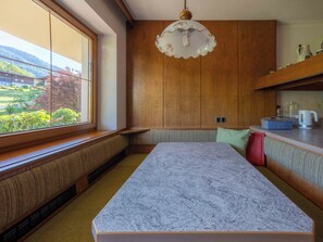 A kitchen with wooden cabinets, a marble countertop, a built-in bench, and a window with a view of greenery. - Villa zur Gondel (Waidring)