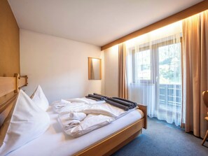 A hotel room with a bed, a wooden headboard, a window with curtains, and a small mirror on the wall. - Villa zur Gondel (Waidring)