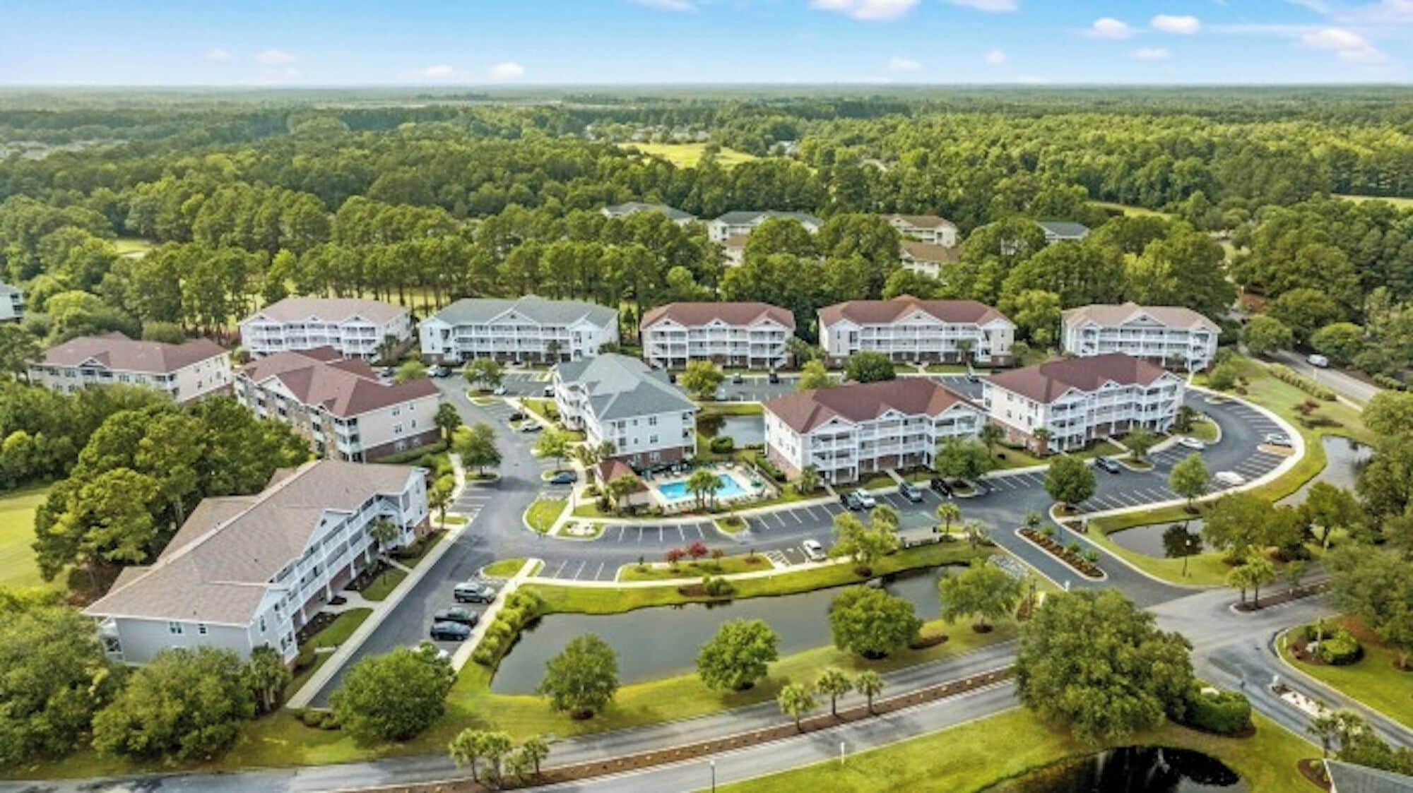 Um bairro residencial com várias casas de dois andares, uma piscina central e um gramado bem cuidado.