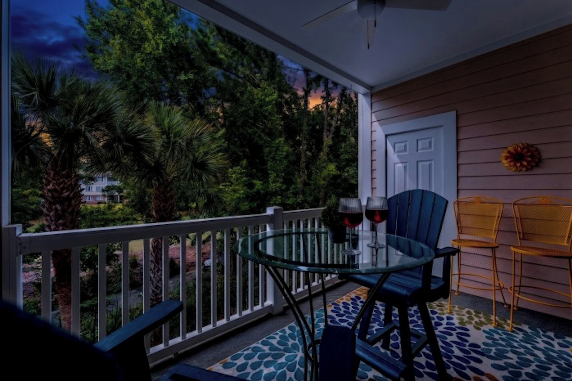 Ein Balkon mit Glastisch und Stühlen, zwei Weingläsern, einer Tür und einem dekorativen Kranz.
