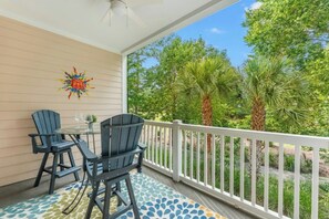 Ein überdachter Balkon mit zwei Adirondack-Stühlen, einem kleinen Tisch und einem dekorativen Sonnenspiegel an der Wand.