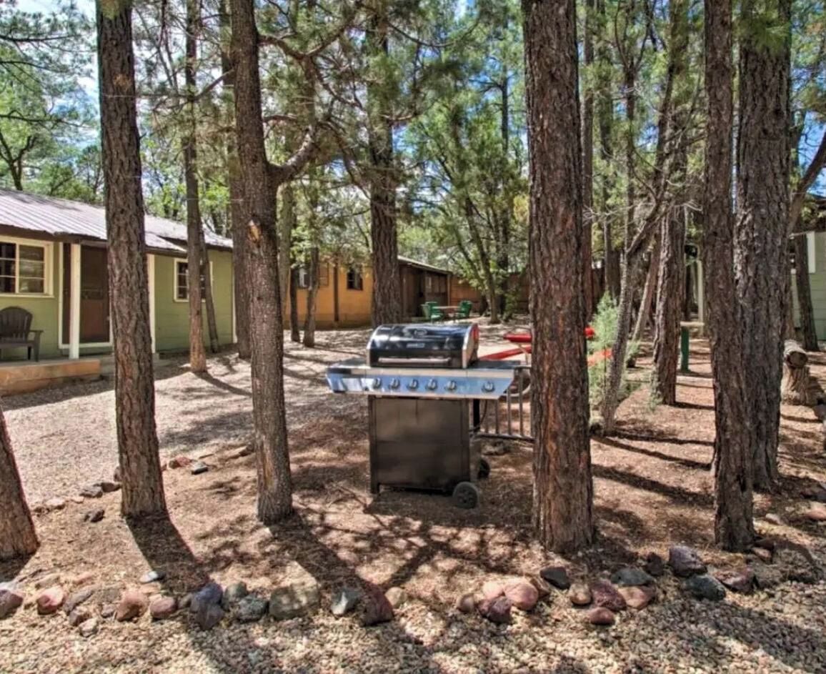 Un barbecue installé dans un espace boisé, avec un bâtiment visible à l’arrière-plan.