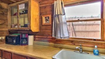 A wooden cabin interior with a kitchen area, including a sink, cabinets, and a window with curtains.