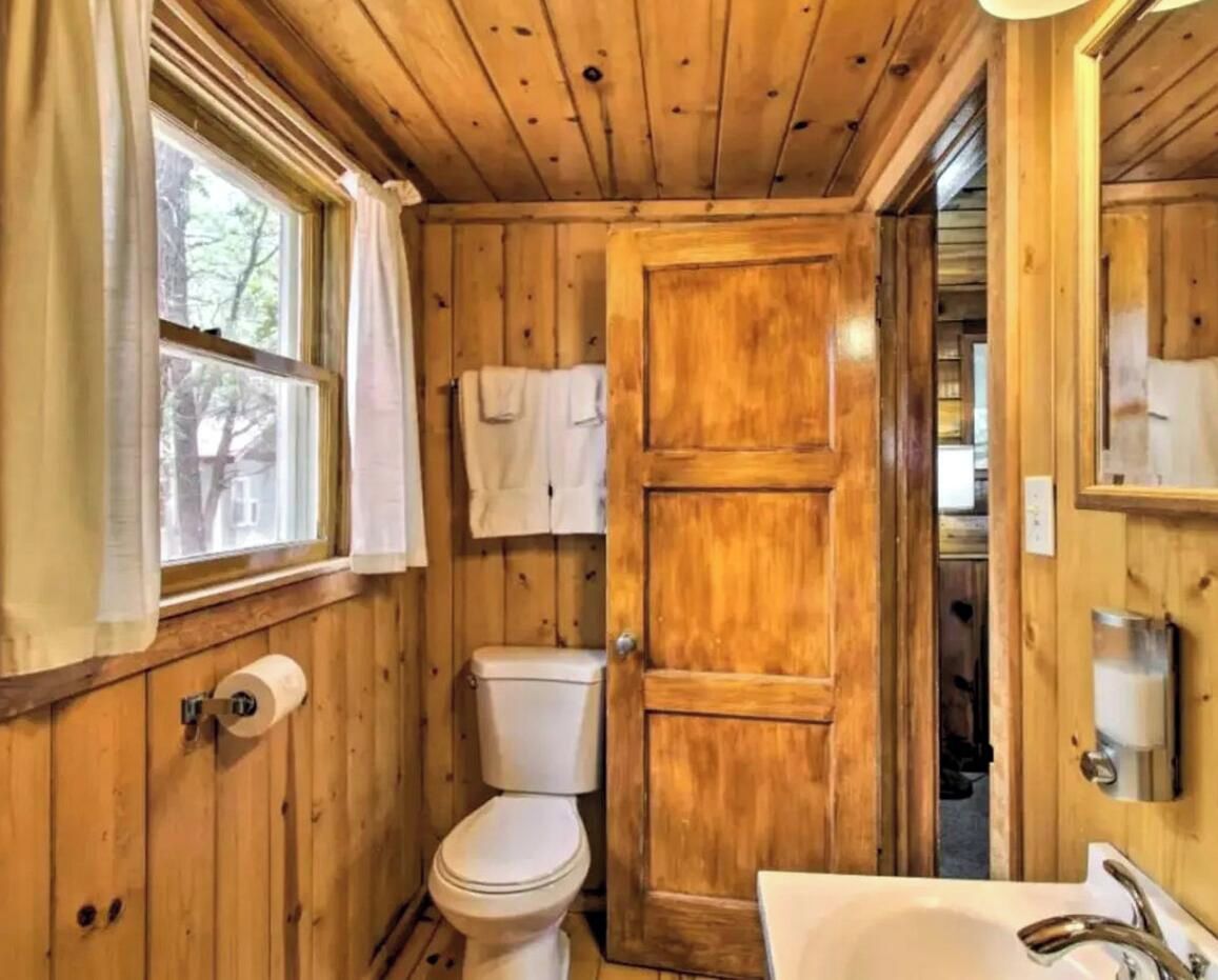 Ein Badezimmer mit Holzwandverkleidung, Toilette, Waschbecken und einer Tür zu einem anderen Raum.