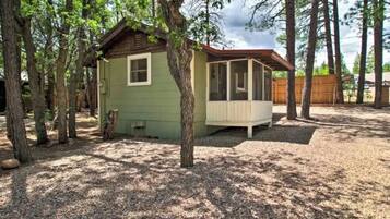 A small cabin with a porch, surrounded by trees and a gravel ground.