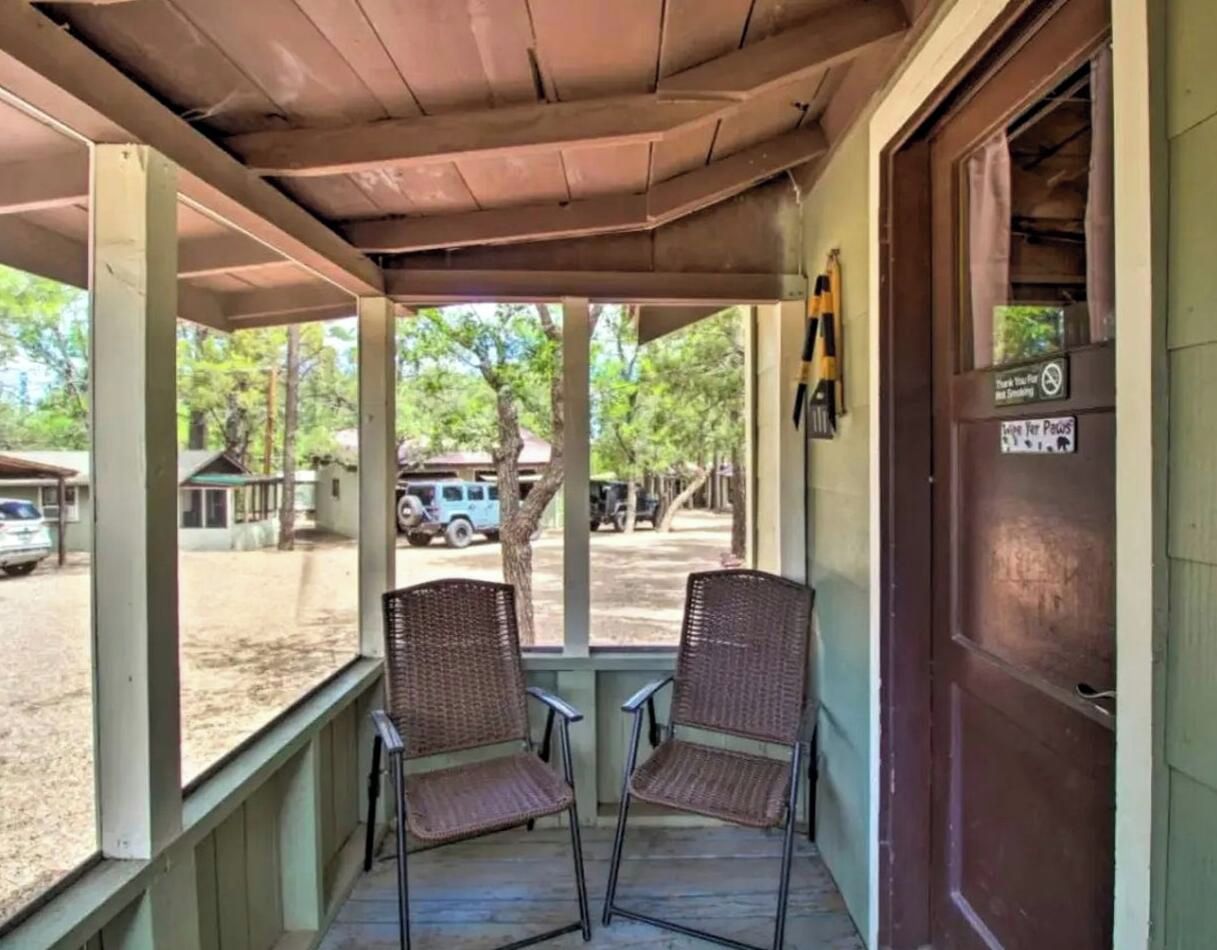 A porch with two wicker chairs, a wooden ceiling, and a view of a parking area with vehicles.