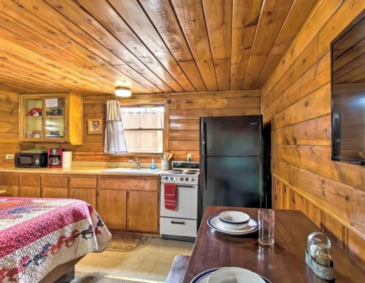 A wooden cabin interior with a bed, kitchenette, and a dining area.