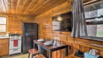 L’intérieur d’un chalet en bois comprend un espace cuisine équipé d’un fourneau, d’un réfrigérateur et d’un coin bar avec des tabourets.