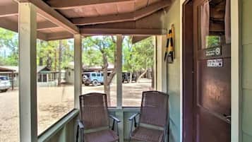 Une véranda avec deux fauteuils en osier, un plafond en bois et une vue sur un parking où sont stationnés des véhicules.