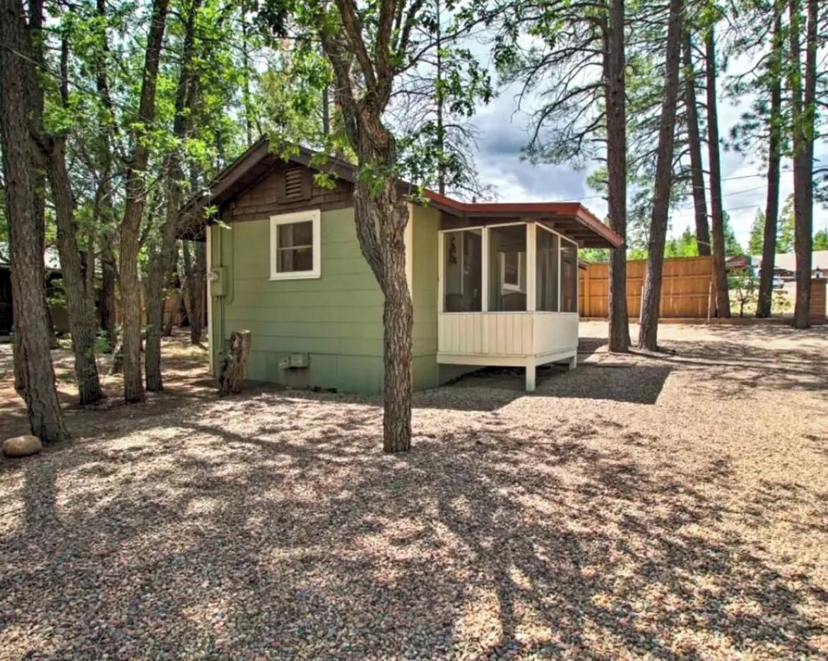 Een kleine hut met een veranda, omgeven door bomen en een grindpad.