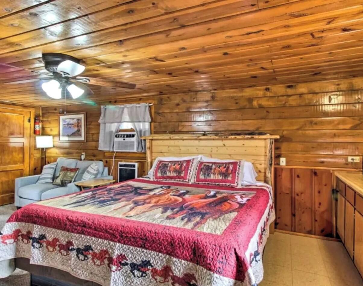 A wooden cabin interior with a bed, a sofa, and a ceiling fan.