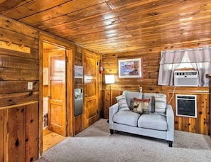 L’intérieur d’un chalet en bois, avec un canapé, un tableau encadré et une fenêtre avec des rideaux.