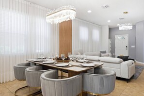 A modern dining area with a rectangular table set for six, surrounded by grey upholstered chairs with gold accents. - Disney Dream Home | Mickey, UP, Harry Potter(2100) (Kissimmee)
