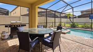 Eine Terrasse im Freien mit einem Glastisch, Korbstühlen, einem Grill und einem Pool.