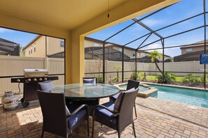 An outdoor patio with a glass table, wicker chairs, a barbecue grill, and a pool. - Disney Dream Home | Mickey, UP, Harry Potter(2100) (Kissimmee)