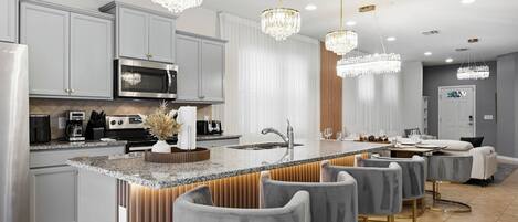 Une cuisine moderne dotée d’un îlot central, de tabourets de bar, d’appareils électroménagers en acier inoxydable et de luminaires suspendus.