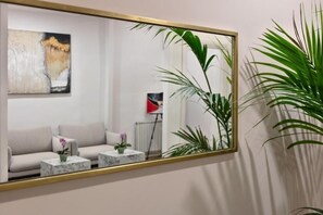 A room with a large mirror, a sofa, two side tables, and a potted plant. - Fellini Design Apartment (Roma)