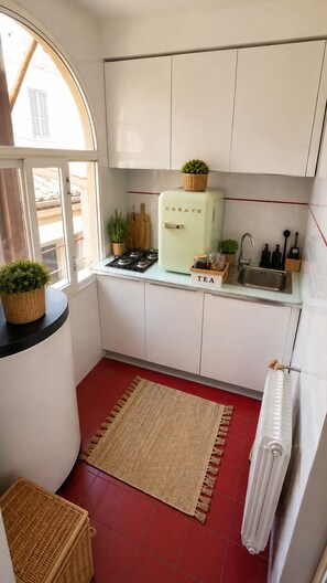 A compact kitchen with white cabinets, a vintage-style refrigerator, a gas stove, a sink, and a window providing natural light. - Fellini Design Apartment (Roma)