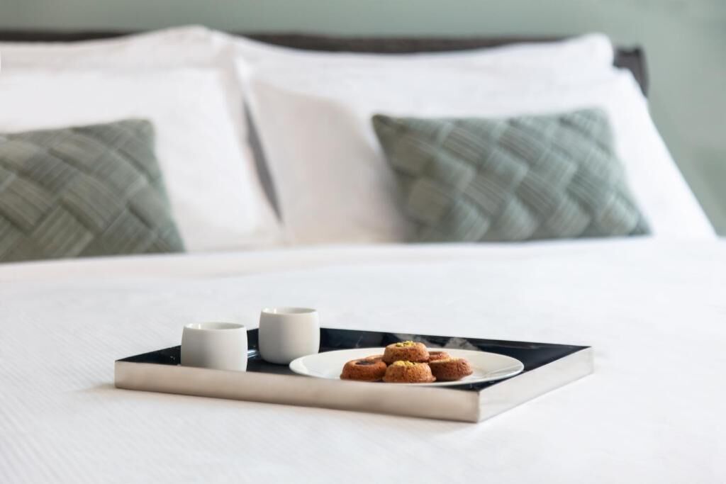 A neatly made bed with a tray of cookies and two cups on a white pillow.