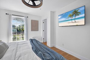 Une chambre à coucher avec un lit, une fenêtre avec des rideaux, un tableau représentant une plage et un radiateur.