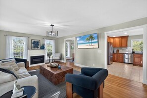 A spacious living room with a fireplace, a dining area, and a kitchen with wooden cabinets. - Elite Living | Kayak | Joy Pool | Outdoor Kitchen ! (Fort Myers)