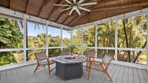 A covered outdoor patio with a fire pit table and chairs, surrounded by large windows and a wooden ceiling. - Elite Living | Kayak | Joy Pool | Outdoor Kitchen ! (Fort Myers)