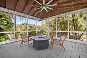 A covered outdoor patio with a fire pit table and chairs, surrounded by large windows and a wooden ceiling. - Elite Living | Kayak | Joy Pool | Outdoor Kitchen ! (Fort Myers)