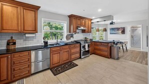 A modern kitchen with wooden cabinets, stainless steel appliances, and a large window providing natural light. - Elite Living | Kayak | Joy Pool | Outdoor Kitchen ! (Fort Myers)