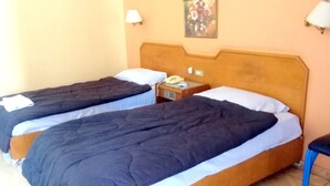 A room with two single beds, each with a pillow and a blanket. There is a nightstand with a phone and a small table between the beds. - New Radwan Hotel Luxor railway (Luxor Governorate)