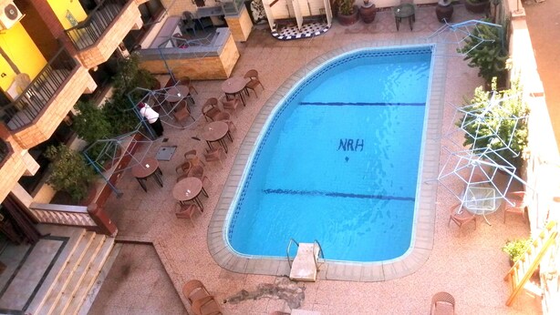 A swimming pool with a sign, surrounded by outdoor seating and a covered area. - New Radwan Hotel Luxor railway (Luxor Governorate)