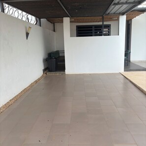 A covered outdoor area with tiled flooring, a trash bin, and a wall with barbed wire. - Keur Béryl House - Somone (Somone)