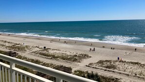 A beach with a clear view of the ocean, sandy shore, and a wooden structure in the background. - Blue Haven by StayMareni - Oceanfront Suite (Myrtle Beach)