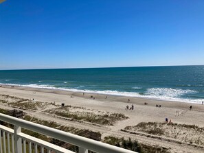 A beach with a clear view of the ocean, sandy shore, and a wooden structure in the background. - Blue Haven by StayMareni - Oceanfront Suite (Myrtle Beach)