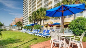 A hotel courtyard with rows of blue lounge chairs and white tables, surrounded by palm trees and a white fence. - Blue Haven by StayMareni - Oceanfront Suite (Myrtle Beach)