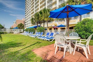 A hotel courtyard with rows of blue lounge chairs and white tables, surrounded by palm trees and a white fence. - Blue Haven by StayMareni - Oceanfront Suite (Myrtle Beach)