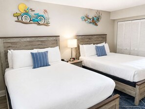 A hotel room with two beds, a nightstand with a lamp, and artwork on the walls. - Blue Haven by StayMareni - Oceanfront Suite (Myrtle Beach)