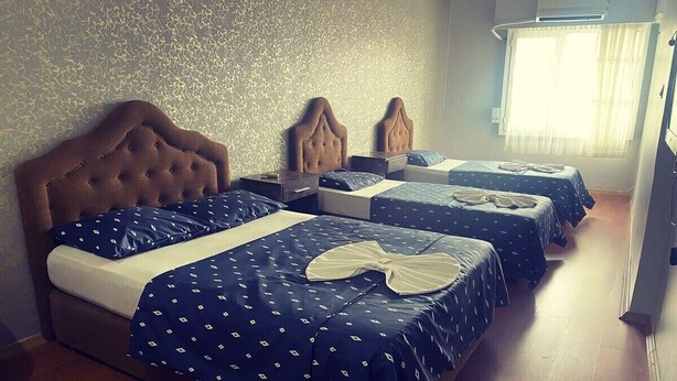 A hotel room with a large bed, two smaller beds, a wooden floor, and a patterned wall. - Benuva Residence (Izmir)