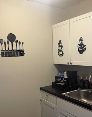 Una cuina amb un adhesiu mural de gots i utensilis de cuina, i un rètol que diu 'KITCHEN', una cafetera i una barra de tapes.