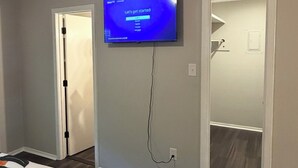 A bedroom with a television mounted on the wall, a bed with a striped blanket, and a door leading to another room.