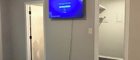 A bedroom with a television mounted on the wall, a bed with a striped blanket, and a door leading to another room.
