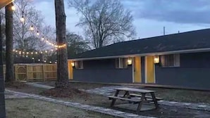 A building with a covered outdoor area, a picnic table, and string lights.