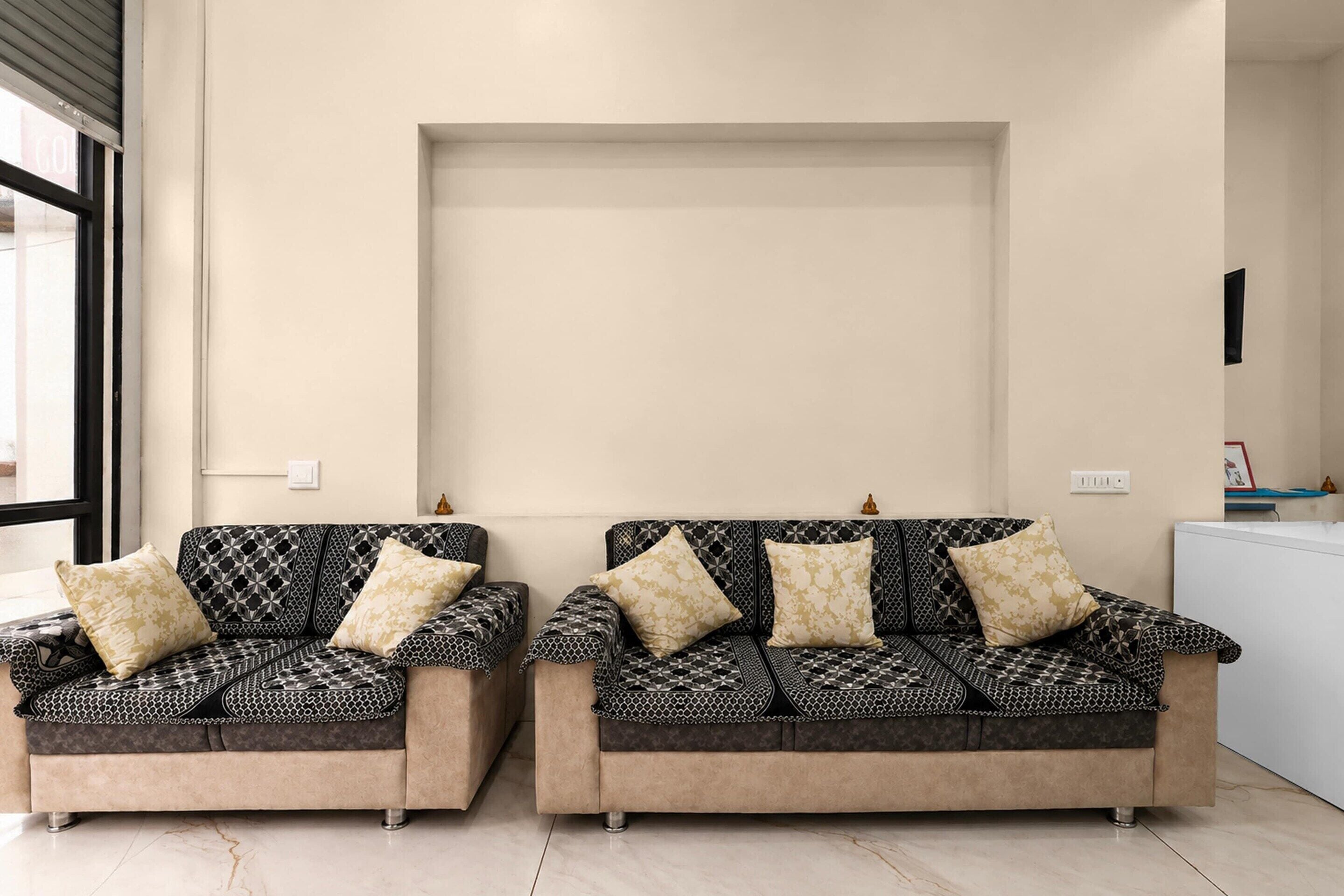 Dos sofás con tapicería estampada y cojines a juego, ubicados en una habitación con pared lisa y una ventana a la izquierda.