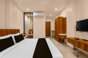A hotel room with a bed, a TV, a desk, and a bathroom visible through a glass door. - Deluxe Golden Retreat Hotel (Anand)