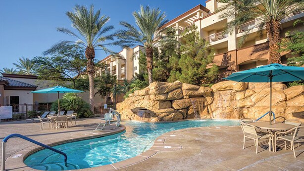 A swimming pool with lounge chairs and umbrellas, surrounded by palm trees and a rocky wall. - Worldmark Boulevard 2-bedroom resort in beautiful Las Vegas (Las Vegas)