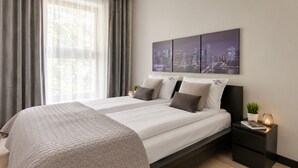 Quarto moderno com vista para a cidade, uma cama com duas almofadas, mesa de cabeceira com abajur e criado-mudo com uma planta.