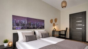 A modern bedroom with a cityscape painting, a bed with white and gray bedding, a desk with a chair, and a dark wooden door. - Sopot Aquarius Bay by Lion Apartments (Sopot)